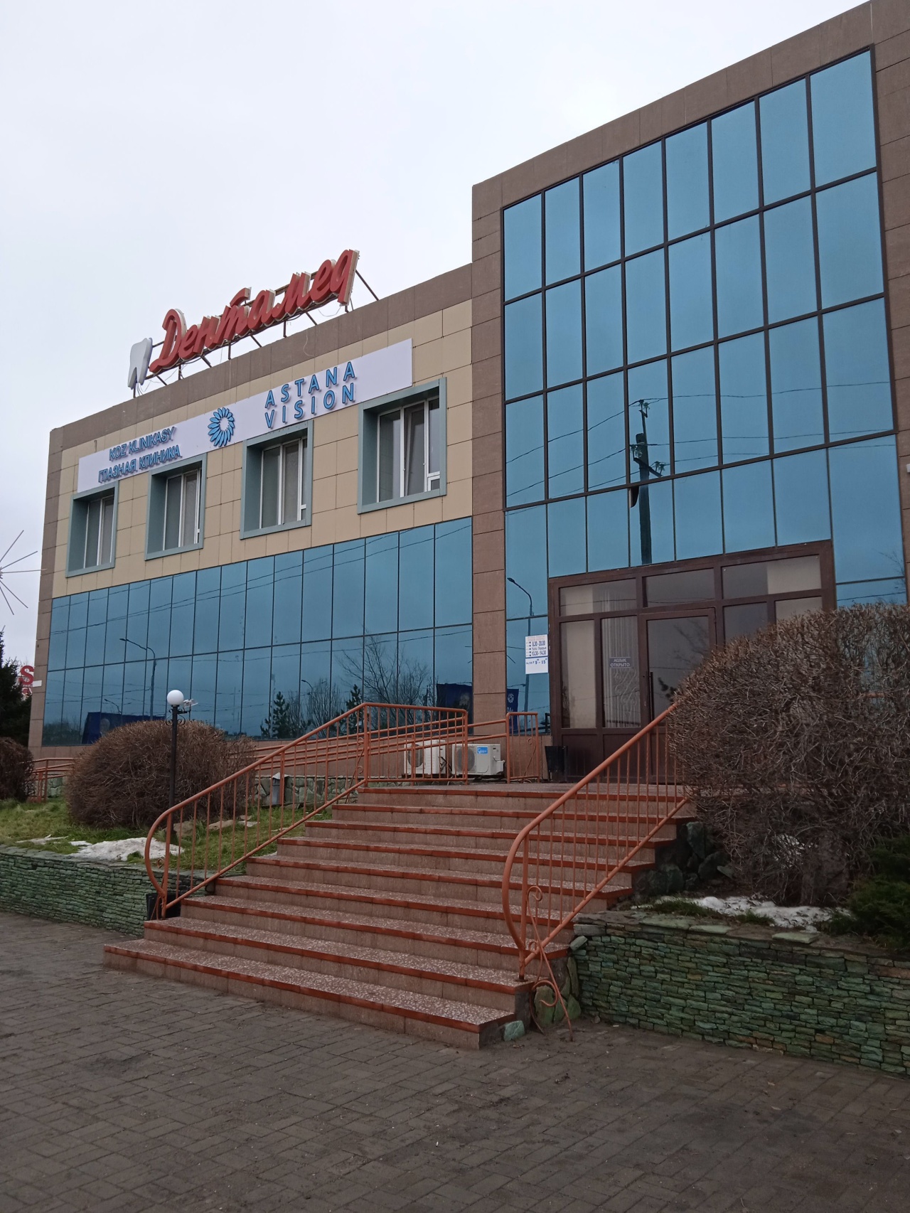 Здание клиники с красной вывеской «Дентамед» на крыше и крыльцом у входа